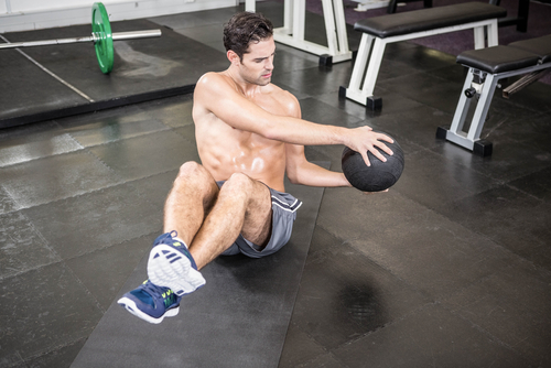 Shirtless man exercising with medicine ball at the gym